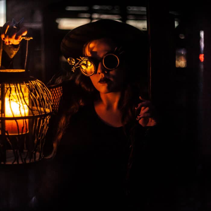 Woman wearing steampunk goggles in the dark carrying a lamp
