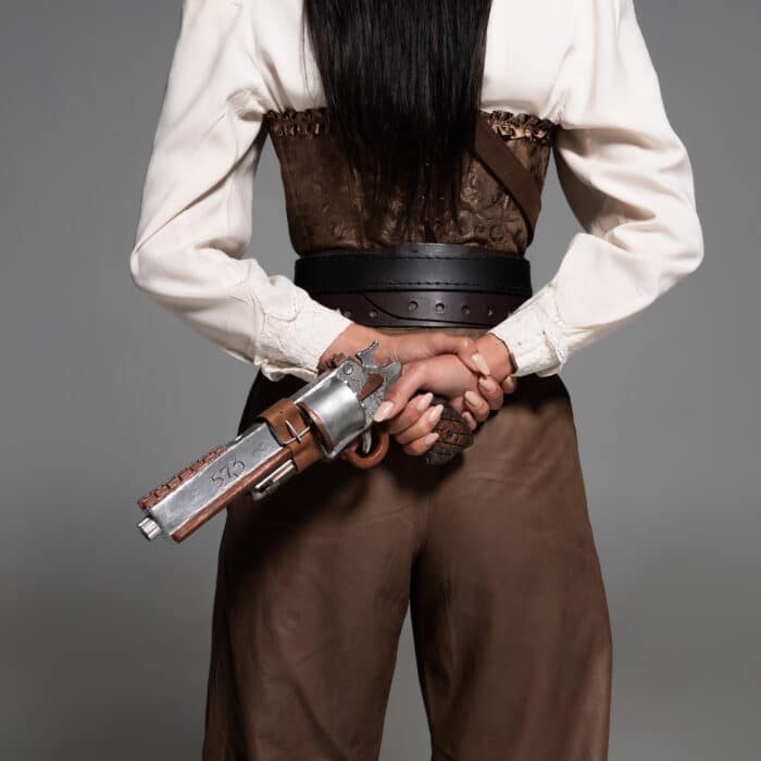Cropped view of steampunk woman holding vintage pistol on grey