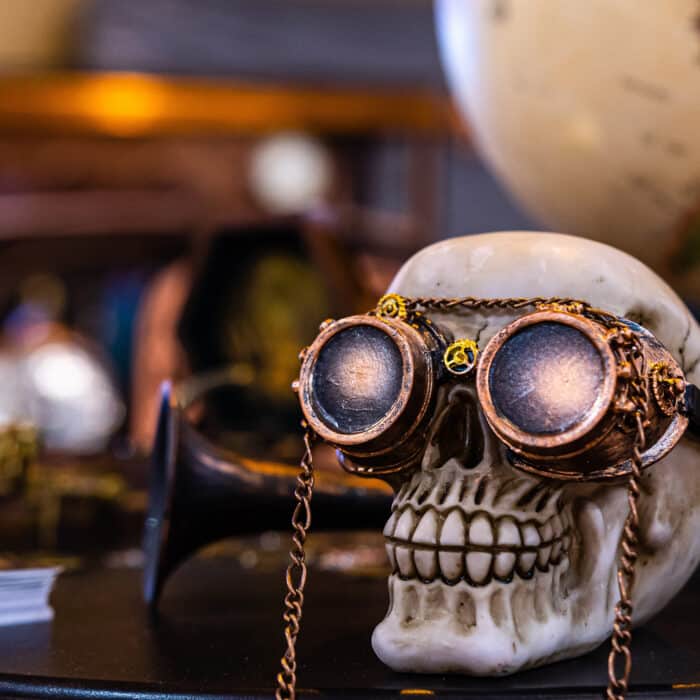 Skeleton head with steampunk glasses on defocused background with globe and old car - image