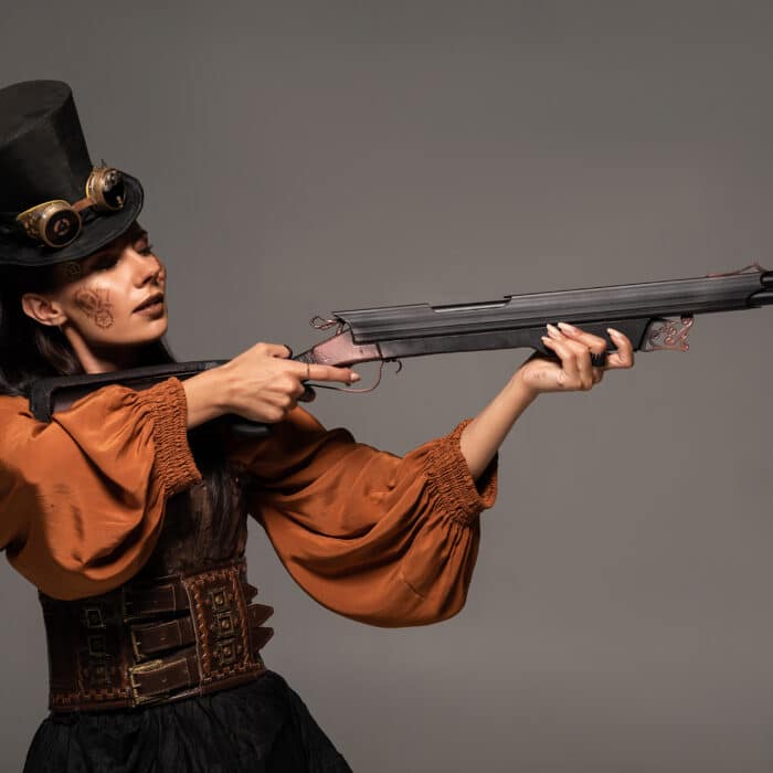 Focused steampunk woman in top hat aiming with gun isolated on grey